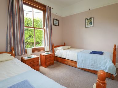 A bedroom with two single beds bedside tables and a window with striped curtains at Beachcliff in Gorran Haven