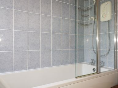 A bathroom with a bathtub shower with blue tiled walls and a glass screen at Beachcliff in Gorran Haven