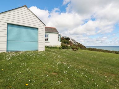 A white house with a blue garage door on a grassy hill overlooking the sea with a picnic table at Beachcliff in Gorran Haven
