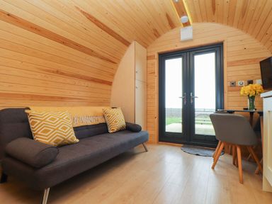 A wooden room with a sofa, pillows, a small table with chairs, and double glass doors at Sun Rise in St Buryan
