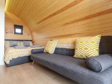 A room with a wooden curved ceiling a bed with yellow and grey bedding and a grey sofa with yellow patterned cushions at Sun Rise in St Buryan