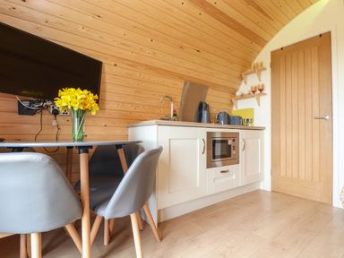 A kitchen area with a wooden wall a table with chairs and a vase of yellow flowers at Sun Rise in St Buryan