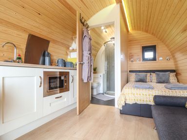 A small wooden room with a kitchenette microwave open door to a bathroom and a bed with yellow patterned bedding at Sun Rise in St Buryan