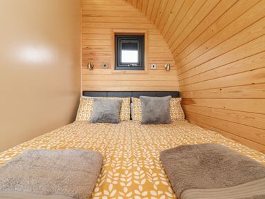 A bedroom with a patterned yellow bedspread gray pillows two towels on bed wood paneled walls and a small window at Sun Rise in St Buryan