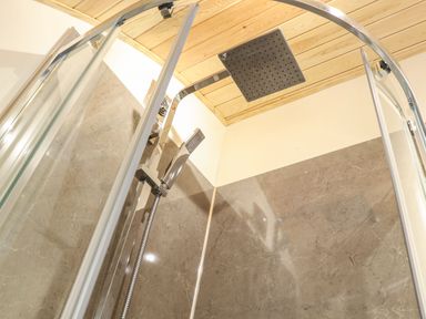 A shower area with a square rainfall showerhead handheld shower and marble wall panels at Sun Rise in St Buryan
