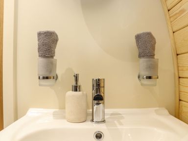 A bathroom sink with a soap dispenser and a chrome faucet with rolled towels in holders on the wall at Sun Rise in St Buryan