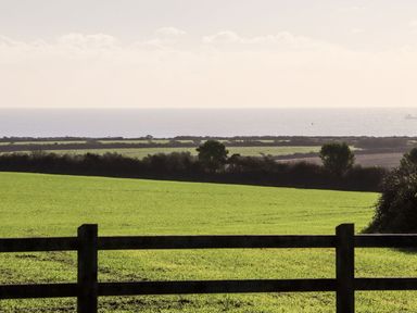 A green field with a wooden fence and hedges with the sea visible in the background at Sun Rise in St Buryan