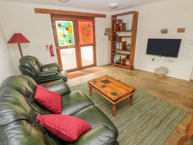 A living room with green leather sofas red cushions a wooden coffee table a floor lamp a wooden shelving unit and a wall-mounted TV at Nook Bethesda near Narberth