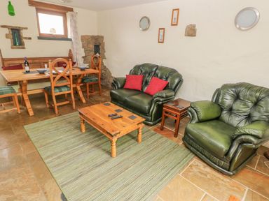 A living room with green leather sofa and armchair wooden coffee table and dining table with chairs at Nook Bethesda near Narberth