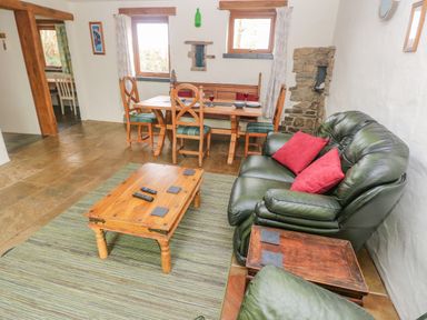 A living area with a green leather sofa red cushions a wooden coffee table with remotes and a dining table with wooden chairs at Nook Bethesda near Narberth