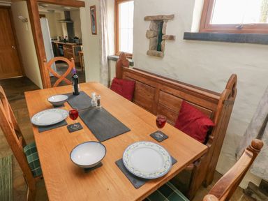 A dining area with a wooden table set with plates bowls glasses and a bottle near a kitchen at Nook Bethesda near Narberth