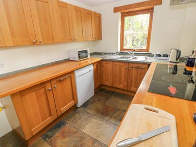 A kitchen with wooden cabinets a countertop a window a sink a dishwasher a toaster an electric kettle and a cutting board with a knife at Nook Bethesda near Narberth