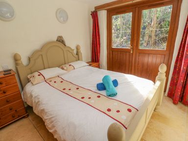 A bedroom with a double bed with white bedding and two rolled towels on top two bedside tables and wooden doors with windows at Nook Bethesda near Narberth