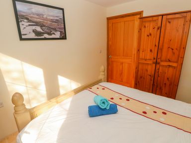 A bedroom with a bed featuring folded towels a wooden door a framed picture on the wall and a wooden wardrobe at Nook Bethesda near Narberth