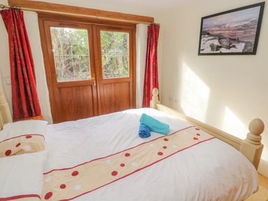 A bedroom with a bed near wooden double doors and red curtains at Nook Bethesda near Narberth