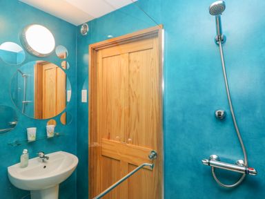 A bathroom with blue walls a wooden door a white sink with soap a shower with a handheld showerhead and round mirrors on the wall at Nook Bethesda near Narberth