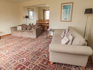 A living room with two sofas a side table a floor lamp and a dining table with chairs at Causeway Cottage in Holy Island