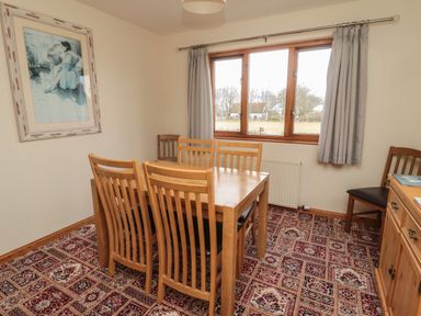 A dining room with a wooden table and six chairs next to a window with grey curtains at Causeway Cottage in Holy Island