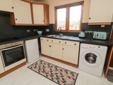 A kitchen with white cabinets a sink washing machine oven refrigerator toaster and kettle at Causeway Cottage in Holy Island
