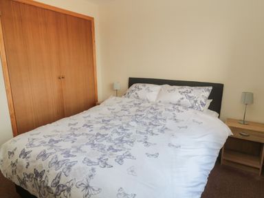 A bedroom with a bed with butterfly bedding a wooden wardrobe and two bedside tables with lamps at Causeway Cottage in Holy Island