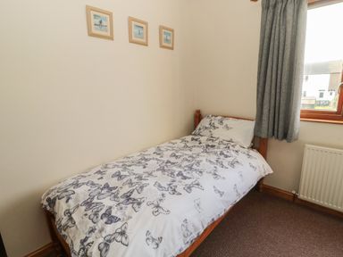 A bedroom with a single bed with butterfly patterned bedding a window with grey curtains and pictures on the wall at Causeway Cottage in Holy Island