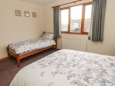 A bedroom with two single beds covered with butterfly patterned bedding and a window with grey curtains at Causeway Cottage in Holy Island