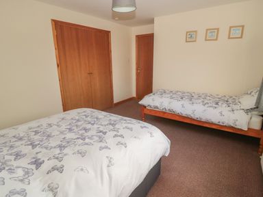 A bedroom with two single beds with butterfly patterned bedding wooden closet and door on a carpeted floor at Causeway Cottage in Holy Island