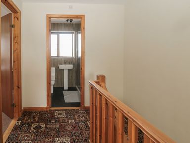 A hallway with patterned carpet leading to a bathroom with a sink and toilet at Causeway Cottage in Holy Island