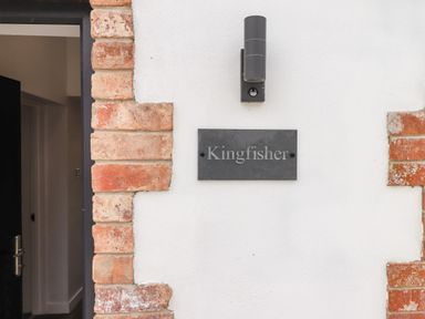A wall with a black outdoor light fixture and a sign that reads Kingfisher next to a partially open door