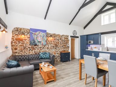 A living room with a gray sofa, wooden coffee table, blue kitchen cabinets, and a dining table with gray chairs at Strawberry Bank - Kingfisher in Pyworthy near Bridgerule