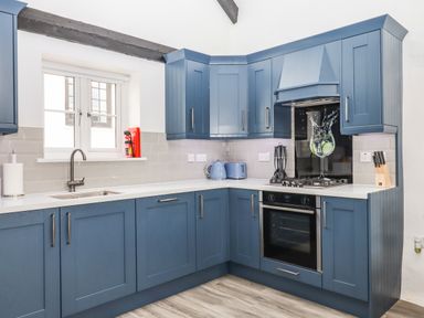A kitchen with blue cabinets a stove a sink under a window and kitchen utensils at Strawberry Bank - Kingfisher in Pyworthy near Bridgerule