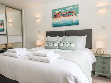 A bedroom with a bed with white linens and folded towels bedside tables with lamps and wall art above the bed at Strawberry Bank - Kingfisher in Pyworthy near Bridgerule