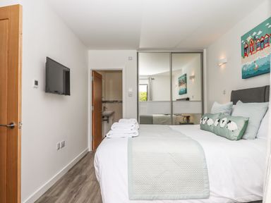 A bedroom with a bed with light bedding a wall mounted tv a door to a bathroom and mirrored sliding wardrobe doors at Strawberry Bank - Kingfisher in Pyworthy near Bridgerule
