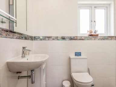 A bathroom with a sink and toilet below a window and tiled walls at Strawberry Bank - Kingfisher in Pyworthy near Bridgerule