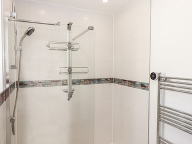 A shower area with a glass panel and chrome showerhead in a bathroom with tiled walls and a chrome towel rail at Strawberry Bank - Kingfisher in Pyworthy near Bridgerule
