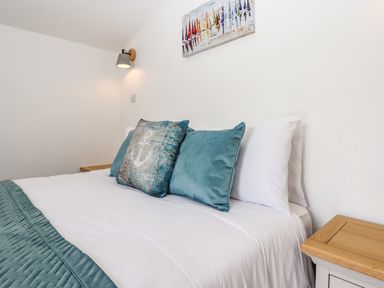 A bed with teal cushions and a wooden side table in a bedroom at Strawberry Bank - Kingfisher in Pyworthy near Bridgerule