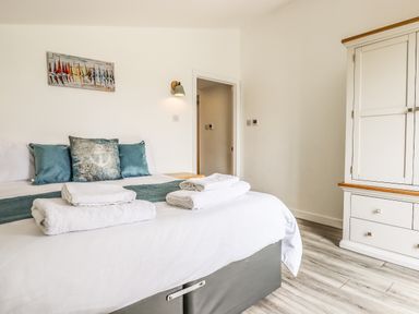 A bedroom with a bed with folded towels pillows wall light wardrobe and wooden floor at Strawberry Bank - Kingfisher in Pyworthy near Bridgerule
