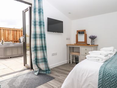 A bedroom with a bed folded towels a dressing table and an open door leading outside at Strawberry Bank - Kingfisher Pyworthy near Bridgerule