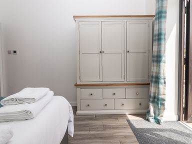 A bedroom with a white wardrobe a bed with towels and a window with plaid curtains at Strawberry Bank - Kingfisher in Pyworthy near Bridgerule