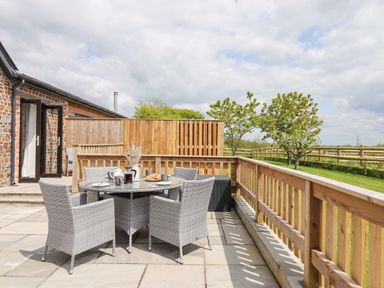An outdoor patio with a round glass table and four wicker chairs at Strawberry Bank - Kingfisher in Pyworthy near Bridgerule
