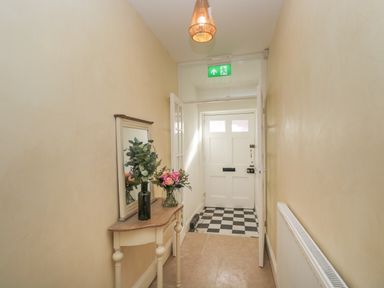 A hallway with a white door a checkered floor a small table with flowers a wall mirror and a radiator at The Hame in Monmouth