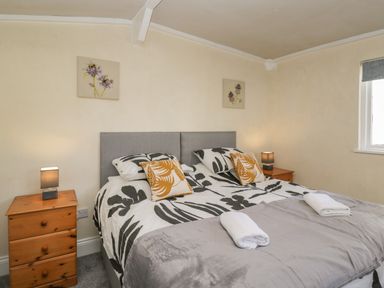 A bedroom with a double bed flanked by wooden bedside tables with lamps and floral artwork above at The Hame in Monmouth