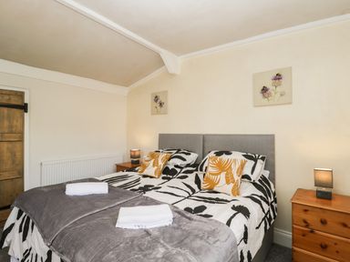 A bedroom with double beds side by side with floral bedding wooden bedside tables with lamps and floral paintings on the wall at The Hame in Monmouth