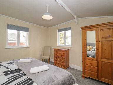 A bedroom with a bed two windows a wooden dresser a wooden wardrobe with mirror and a chair at The Hame in Monmouth
