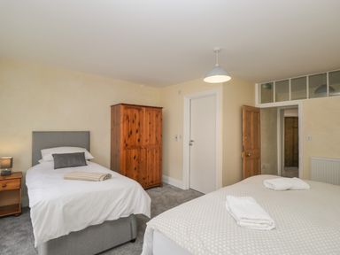 A bedroom with a single bed and a double bed with folded towels on them a wooden wardrobe a bedside table with a lamp and two doors at The Hame in Monmouth