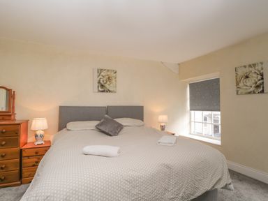 A bedroom with a large bed two bedside tables with lamps a window and wooden drawers at The Hame in Monmouth