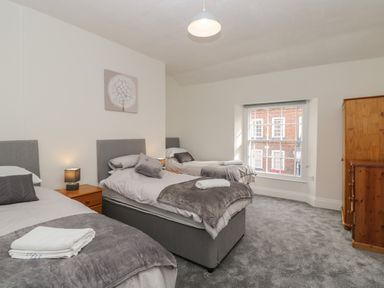 A bedroom with three single beds gray bedding a wooden dresser a window and a painting at The Hame in Monmouth