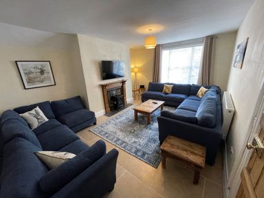 A living room with two blue sofas a wooden coffee table a fireplace with a TV above and a patterned rug at The Hame in Monmouth