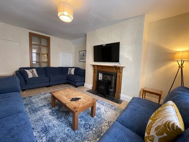 A living room with blue sofas a wooden coffee table a fireplace with a mounted television and a standing lamp at The Hame in Monmouth