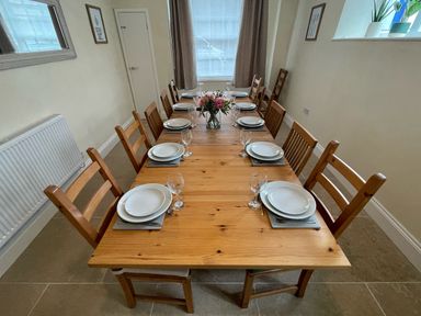 A dining room with a wooden table set for ten with plates glasses cutlery and flowers at The Hame in Monmouth